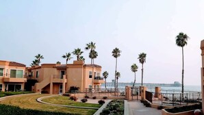 Un hôtel en bord de mer, composé de bâtiments à plusieurs étages, bordé de palmiers et offrant une vue sur l’océan.