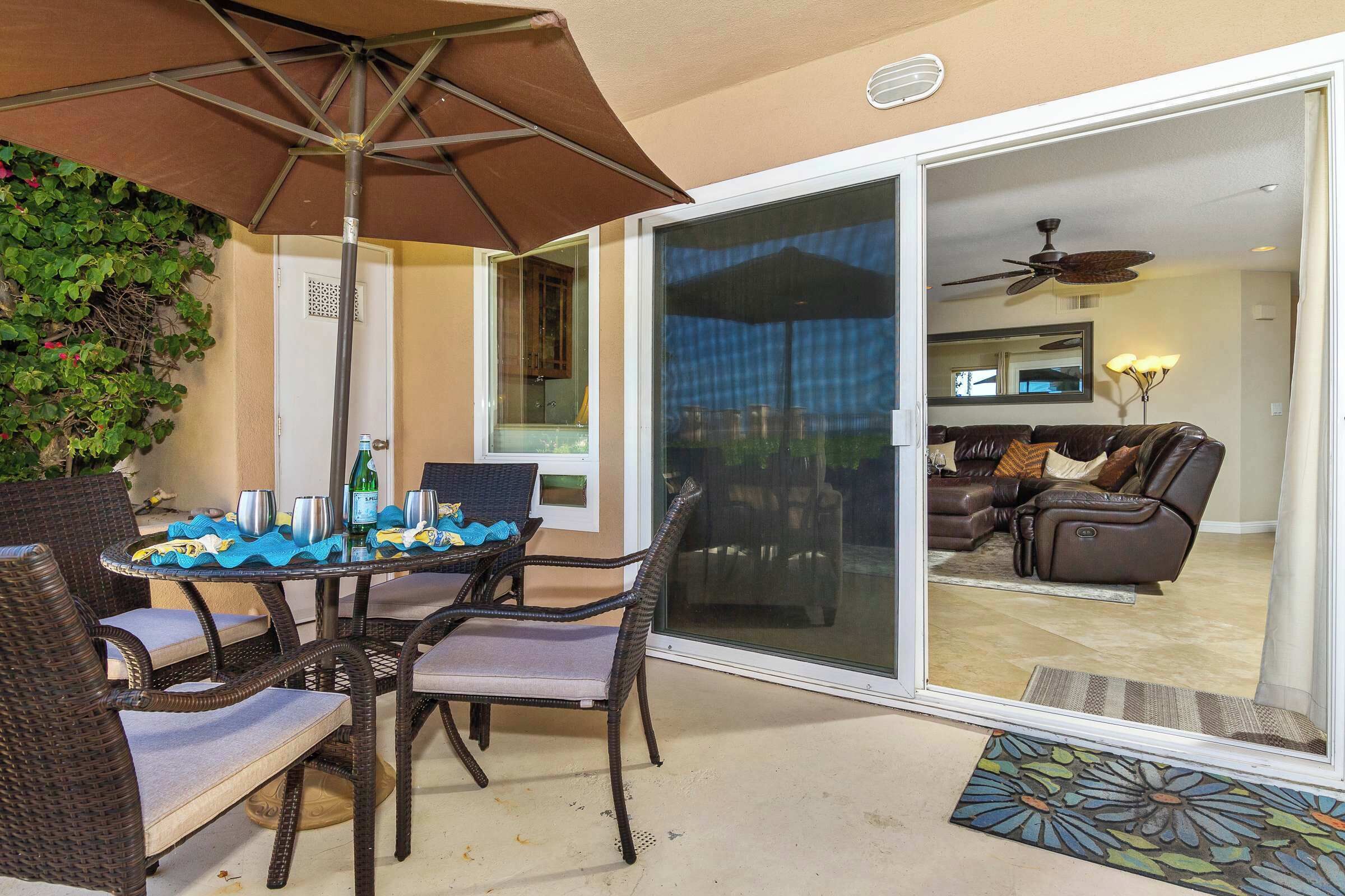 Un espace patio aménagé avec des meubles en osier, une table dressée avec des verres et une bouteille, et un ventilateur de plafond visible au fond.