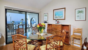 A dining area with a glass table surrounded by wooden chairs, a vase with flowers, and framed pictures on the wall. - 152-4 Coastal Luxury with Panoramic Ocean View (Oceanside)