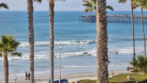 A beach with palm trees, a pier, and people walking along the shore. - 152-4 Coastal Luxury with Panoramic Ocean View (Oceanside)