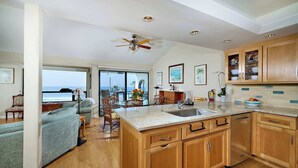 A spacious kitchen with wooden cabinets, a large island with a sink, and a view to the outside. - 152-4 Coastal Luxury with Panoramic Ocean View (Oceanside)