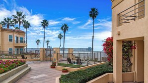 A courtyard with palm trees, a pool, and a building with a balcony. - 5N-31 Beach View, BBQ & Jacuzzi! (Oceanside)