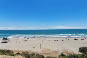 Een strand met een rederspost en heldere lucht, en een rustige zee.