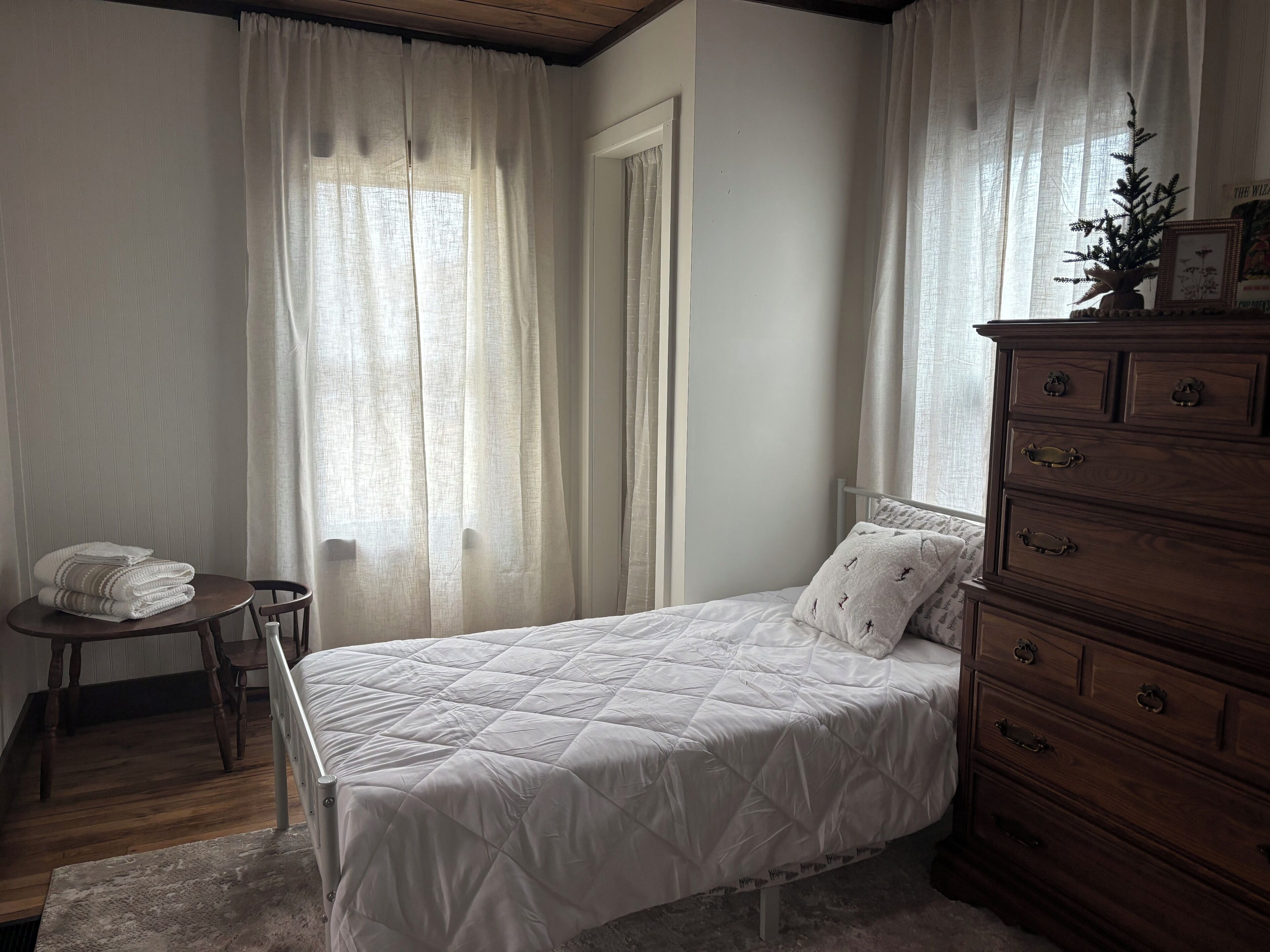 A bedroom with a bed, a wooden dresser, a chair, and a small table.