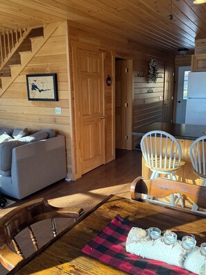 Ein gemütliches Blockhaus-Interieur mit einer Holztreppe, einem Essbereich mit Tisch und Stühlen, einer Couch und einem Kühlschrank.