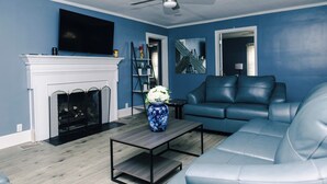 Un salon avec une cheminée, un canapé bleu, une table basse et un ventilateur de plafond.
