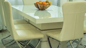 A dining area with a white table and chairs, a bowl of fruit, and sheer curtains.