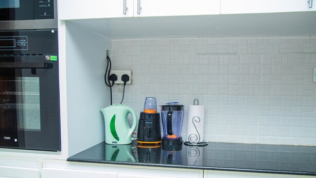 A kitchen with a microwave, a kettle, a blender, and a paper towel holder on the counter.