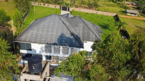 A large house with a sloped roof, surrounded by greenery and a fenced yard.