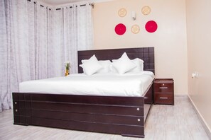 A bedroom with a dark wooden bed, white bedding, a nightstand with drawers, and a wall with decorative items.