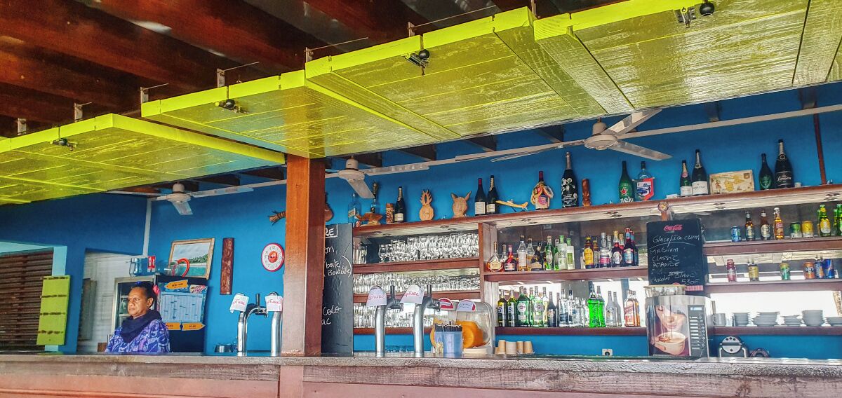 A bar with shelves of bottles and glasses, a chalkboard menu, and a person behind the counter.