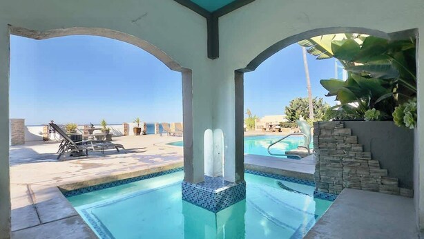 A swimming pool with a clear view of the sky and a lounge area with chairs and a table. - Oceanfront Rosarito Balcony, Beach & Amazing Sunsets (Playas de Rosarito)