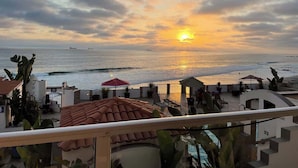 A balcony with a view of the ocean at sunset, outdoor seating, and a red umbrella. - Oceanfront Rosarito Balcony, Beach & Amazing Sunsets (Playas de Rosarito)