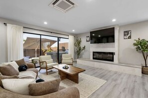 Ein modernes Wohnzimmer mit einer Couch, Sesseln, einem Couchtisch, einem Kamin und einem Fernseher.