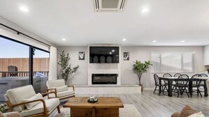 A modern living room with a fireplace, a dining area, and a balcony with outdoor furniture. - Wellness Bnb - Your San Diego Retreat! (San Diego)