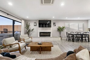 Ein modernes Wohnzimmer mit Kamin, Essbereich und Balkon mit Gartenmöbeln.