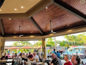 An outdoor dining area with wooden ceiling beams, tables, and chairs. - AVAILABLE 2026 SEASON! Treviso Bay Resort Beautiful 3 Bedroom Lake View Condo (Naples)