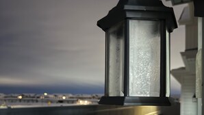 A balcony with a wooden railing, a lantern, and a view of a snowy landscape with distant lights. - YEG keswick townhouse retreat (edmonton)