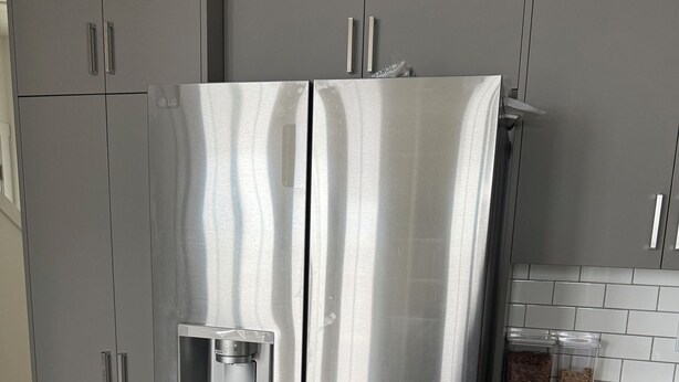 A stainless steel refrigerator with a water dispenser, situated in a kitchen with grey cabinets and a tiled backsplash. - YEG keswick townhouse retreat (edmonton)