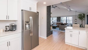 Una cocina moderna con armarios blancos, un refrigerador de acero inoxidable y una cafetera.