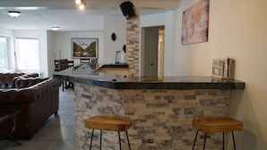Una cocina moderna con protector contra salpicaduras de piedra, dos taburetes de bar de madera y un comedor con sofá de cuero y mesa.