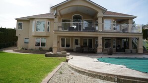 Una casa de dos pisos con balcón, piscina techada y césped cuidado.