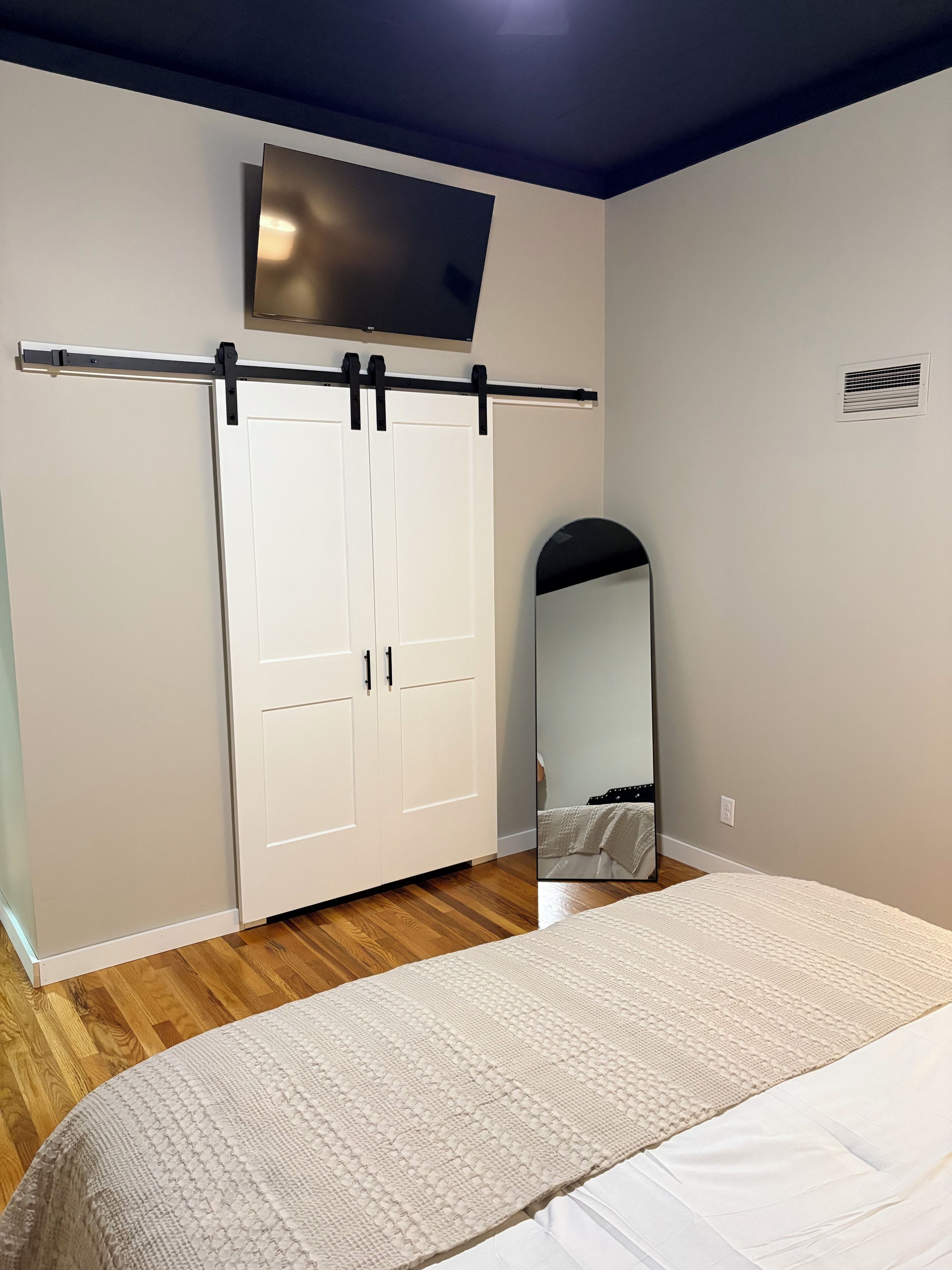 Un dormitorio con cama, armario, televisor de pantalla plana montado en la pared y espejo.