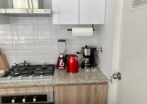 A kitchen with a gas stove, a red kettle, a blender, a coffee maker, and a roll of paper towels on the counter. - Modern 2-Bedroom Apartment in Miraflores | King-Size Bed & Terrace with Park Views (Miraflores)