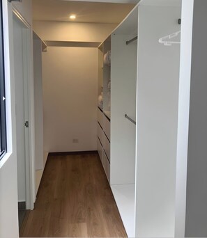 A narrow hallway with wooden flooring, white walls, and a white wardrobe with a hanging rack. - Modern 2-Bedroom Apartment in Miraflores | King-Size Bed & Terrace with Park Views (Miraflores)