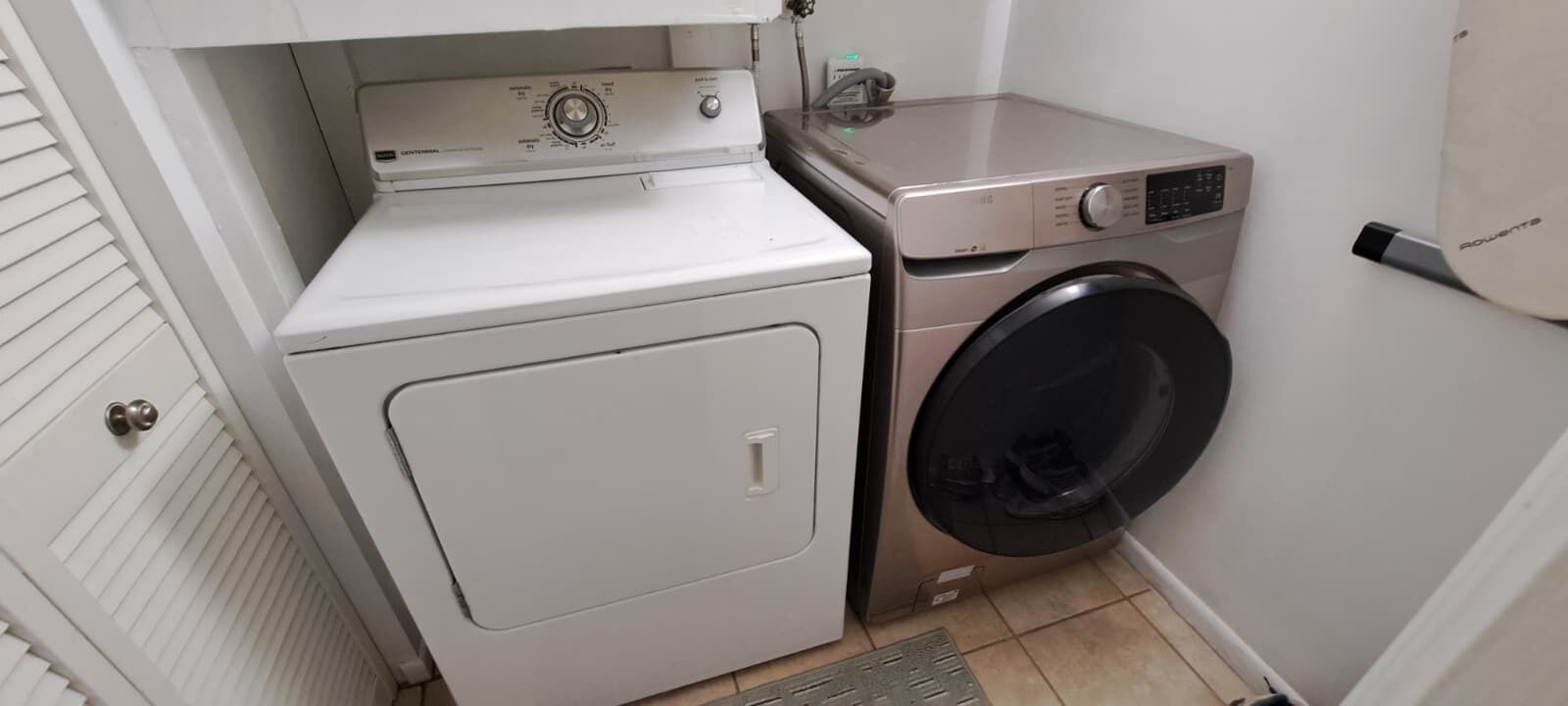 Un área de lavandería compacta con lavadora y secadora de carga frontal, un estante pequeño sobre la secadora, y una puerta con pomo.