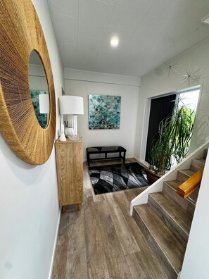 Ein modernes Interieur mit Holzboden, einem runden Spiegel, einer Bank, einem Gemälde und einer Treppe.