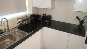 Een keuken met een dubbele spoelbak, een zwart aanrecht, witte kasten en een raam dat voor natuurlijk licht zorgt.