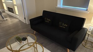 Een moderne woonkamer met een zwarte bank, een glazen salontafel en een witte vloerkleed.