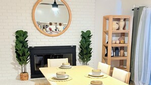 Een eetgedeelte met een houten tafel voor vier personen, een bank en twee potplanten.