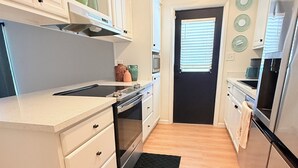 Een compacte keuken met witte kastjes, een zwart aanrecht, een ingebouwde oven en een roestvrijstalen koelkast.