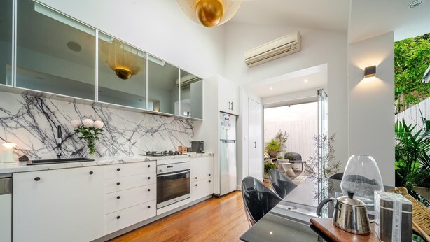 Una cocina moderna con armarios blancos, salpicadero de mármol y un comedor con mesa y sillas de vidrio.