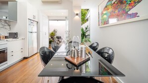 Una cocina moderna con zona de comedor, que presenta una mesa de vidrio, sillas negras y un cuadro abstracto colorido en la pared.