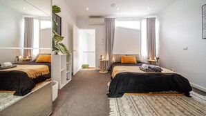 Habitación de hotel moderna con dos camas, un espejo grande, una planta pequeña y vista al pasillo.