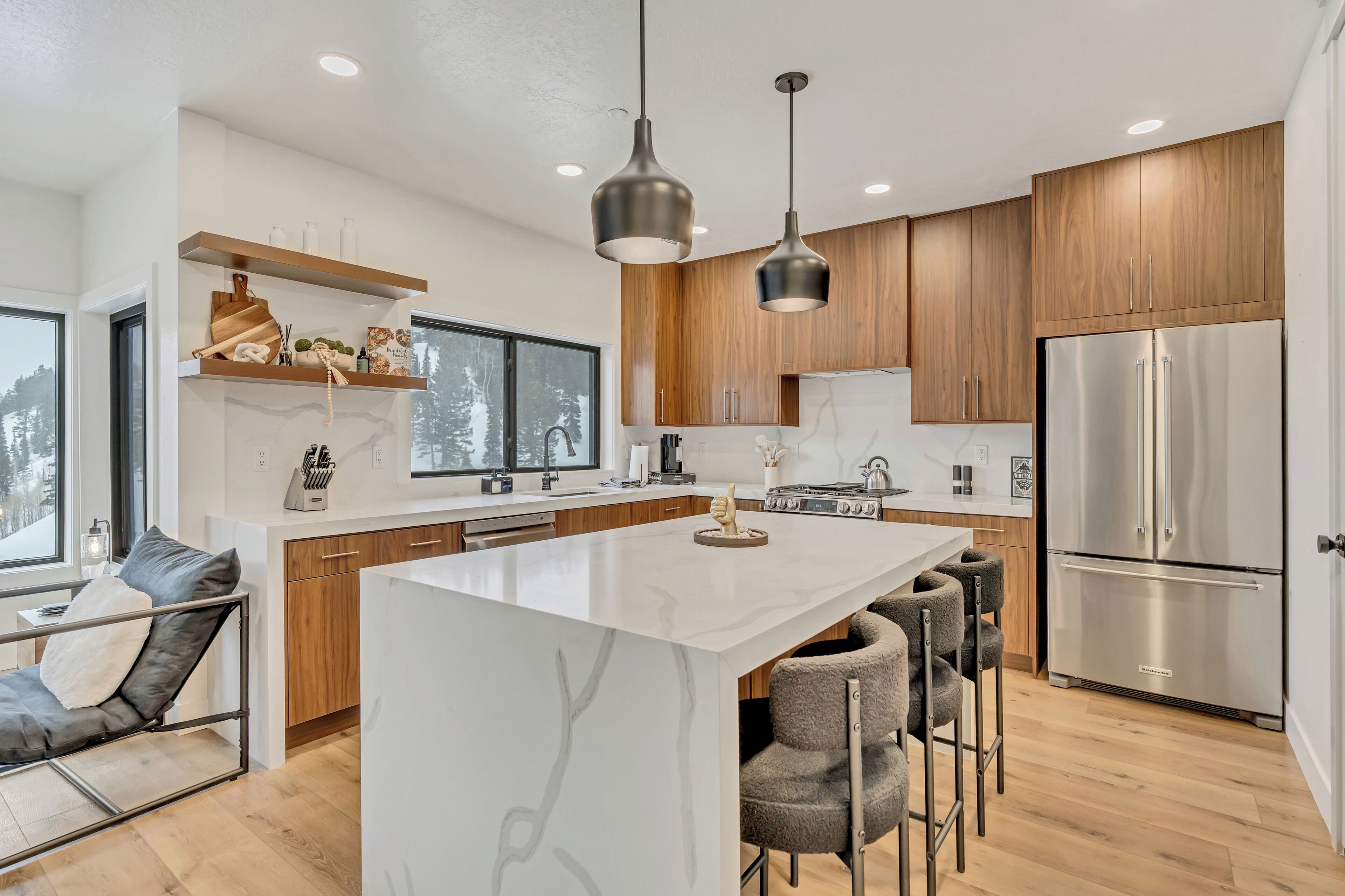 A modern kitchen with a central island, wooden cabinets, stainless steel appliances, and pendant lighting.