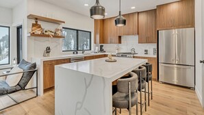 Una cocina moderna con una isla central, armarios de madera, electrodomésticos de acero inoxidable e iluminación colgante.