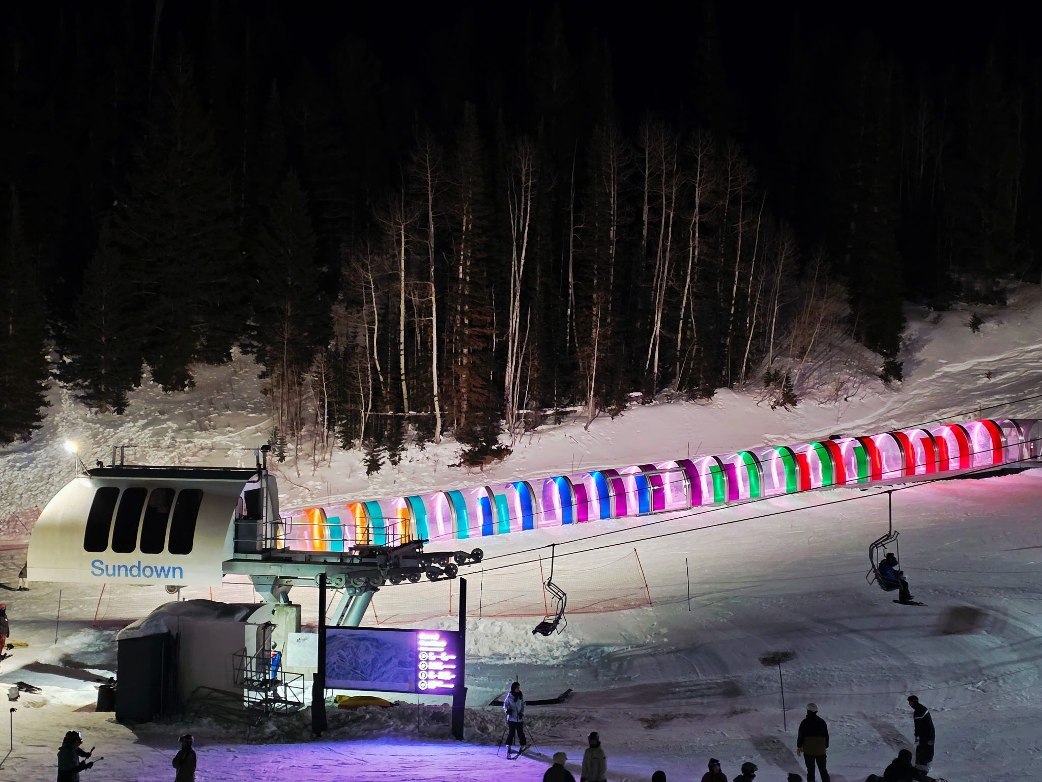 Un télésiège avec des cabines aux couleurs vives et un panneau indiquant « Sundown ».