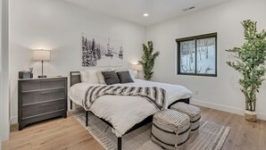 Un dormitorio moderno con una cama grande, mesitas de noche, un ventanal con vistas a árboles y una planta en maceta.