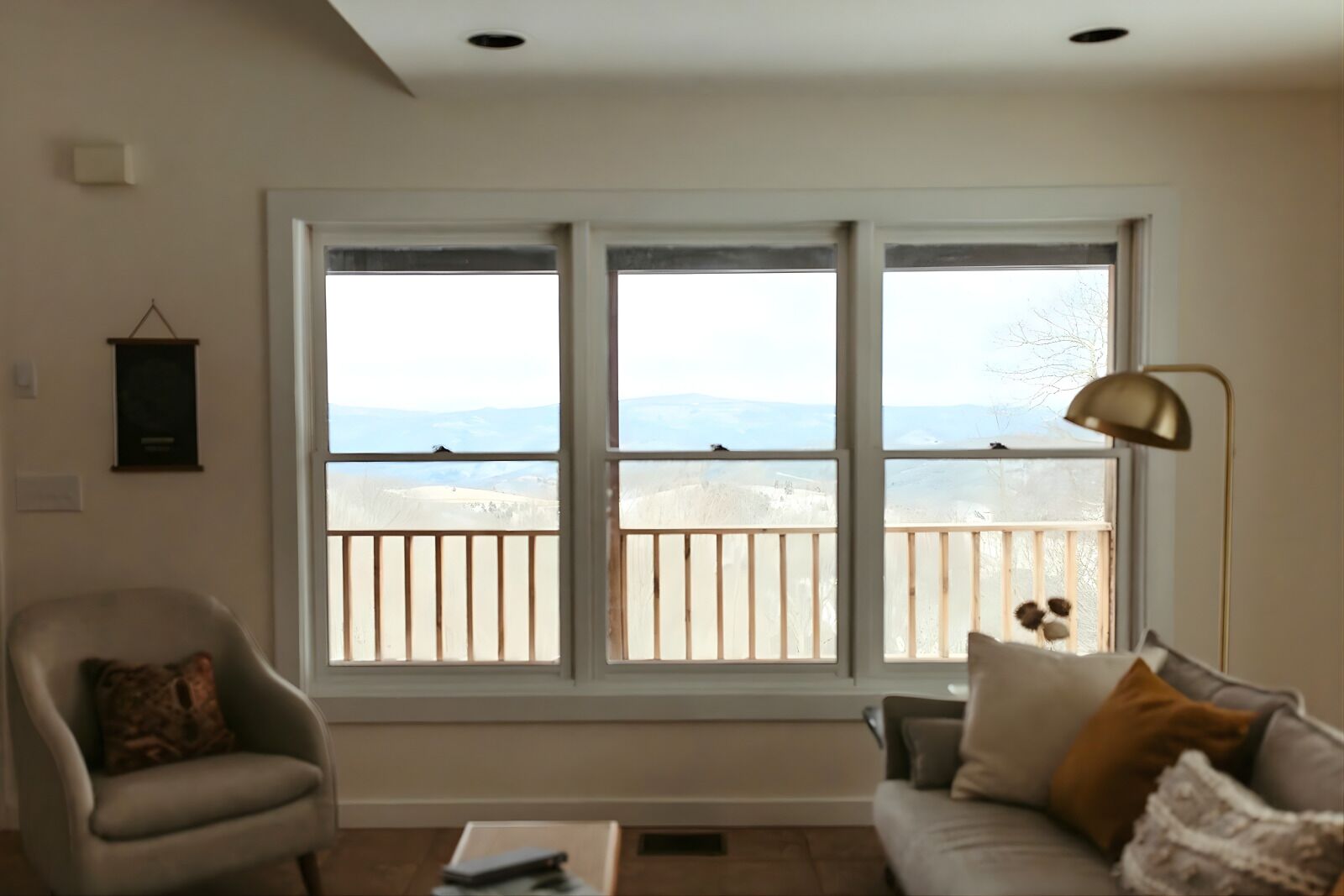 A living room with a large window overlooking a snowy landscape, a sofa, a chair, and a floor lamp.