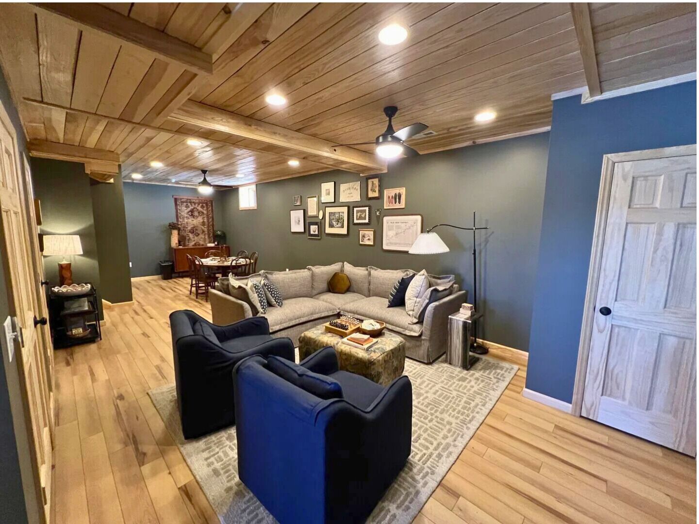 A cozy living room with a wooden ceiling, a sofa set, a coffee table, and a dining area in the background.