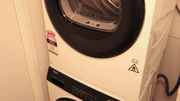A front-loading Haier washer and dryer stacked in a laundry room. - Seaside Getaway Large Private Courtyard - Parking (Surfers Paradise)