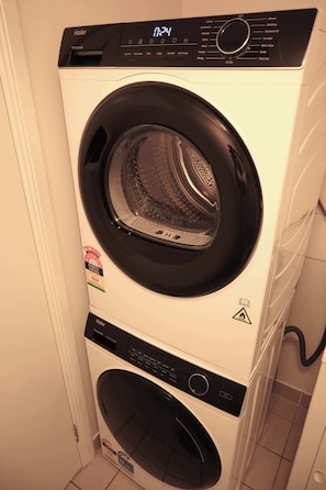 A front-loading Haier washer and dryer stacked in a laundry room. - Seaside Getaway Large Private Courtyard - Parking (Surfers Paradise)
