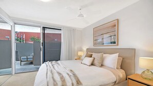 A bedroom with a bed, a nightstand, a lamp, a ceiling fan, and a sliding glass door leading to an outdoor area. - Seaside Getaway Large Private Courtyard - Parking (Surfers Paradise)