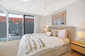 Ein Schlafzimmer mit einem Bett, einem Nachttisch, einer Lampe, einem Deckenventilator und einer Glasschiebetür, die zu einem Außenbereich führt.