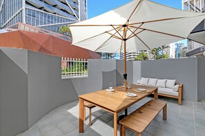 Eine Terrasse im Freien mit einem Holztisch, Bänken, einem weißen Sonnenschirm und einer weißen Couch.