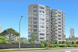 Um edifício residencial com vários andares, varandas, uma rua em frente e céu aberto.